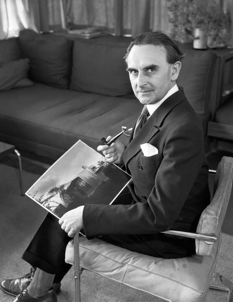 Richard Neutra holding a photo of the Beard House in Altadena, By Los Angeles Times - https://digital.library.ucla.edu/catalog/ark:/21198/zz002cwx90, CC BY 4.0, https://commons.wikimedia.org/w/index.php?curid=121595117